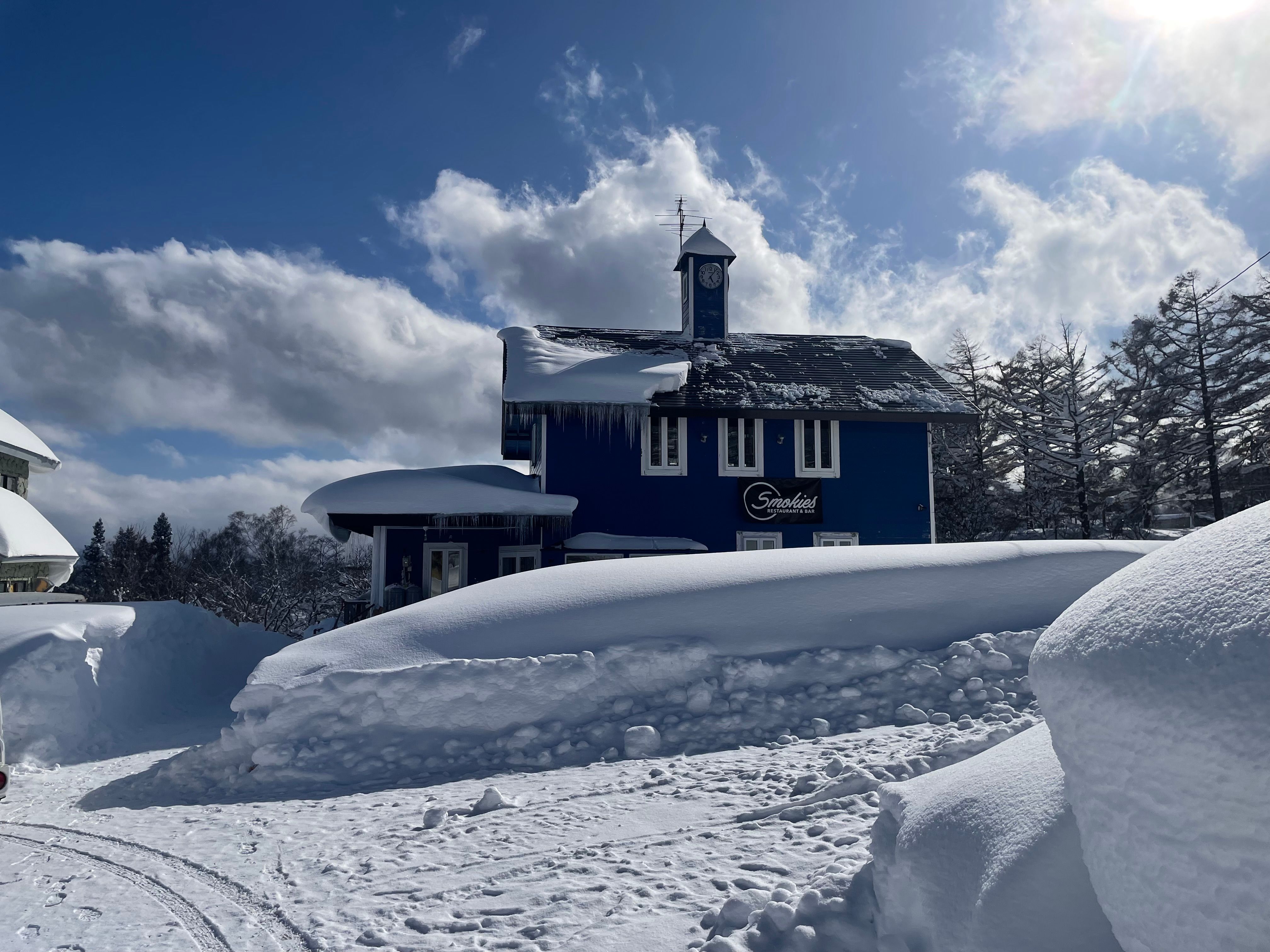 The blue Smokies building in falling snow, with a snow loader clearing the road