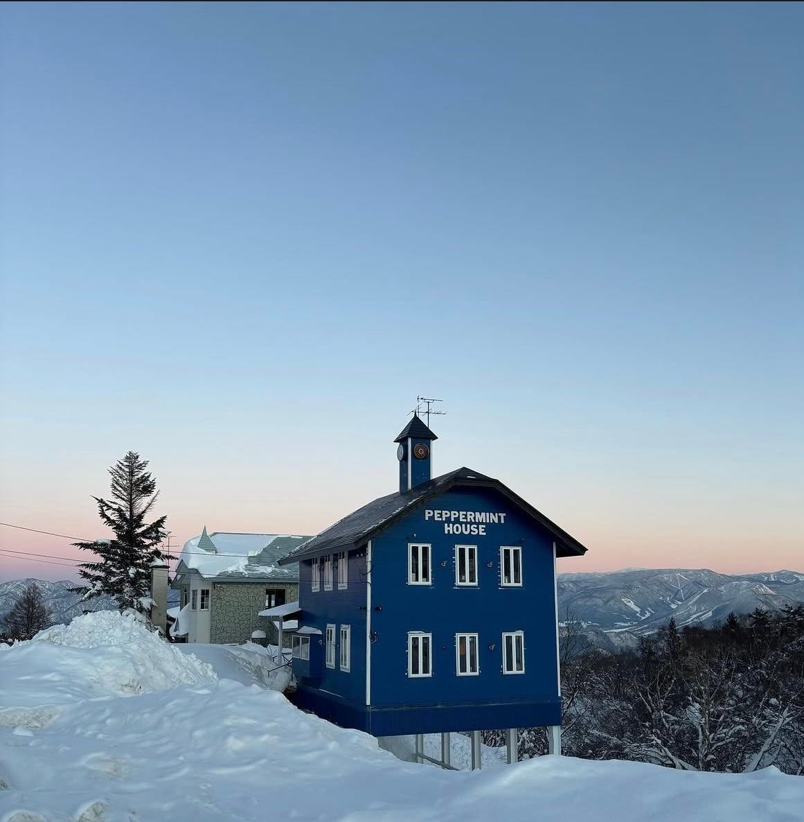 夕暮れの山々を背にした、時計塔のある青い建物